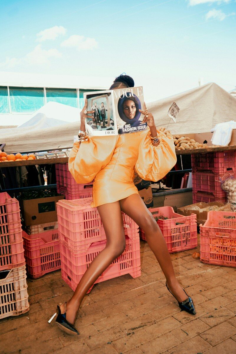Photo by Christian Agbede A person in a yellow dress holding a Vogue magazine in a market